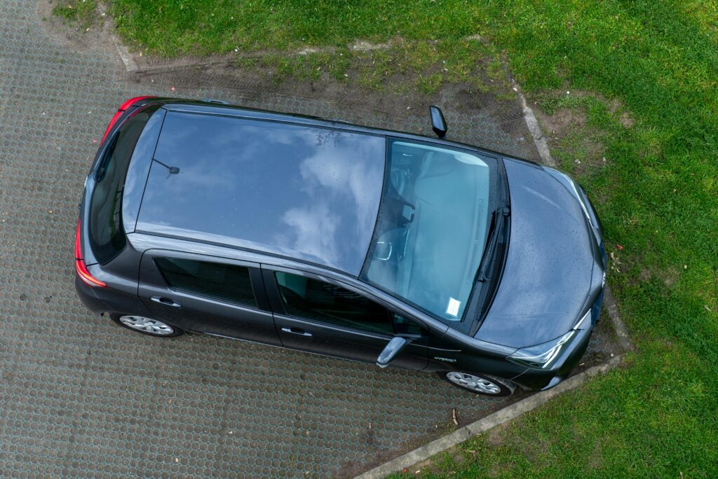 Top view of a black car parked on a grass and concrete surface, showcasing its exterior design.